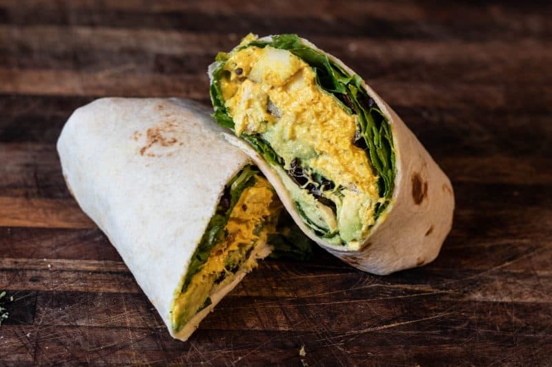 Curry chicken salad in wrapped in a tortilla, spring mix, and sliced avocado.