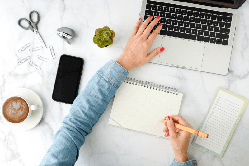 Woman with one hand on her computer and another with a pencil getting ready to write down her smart goals.