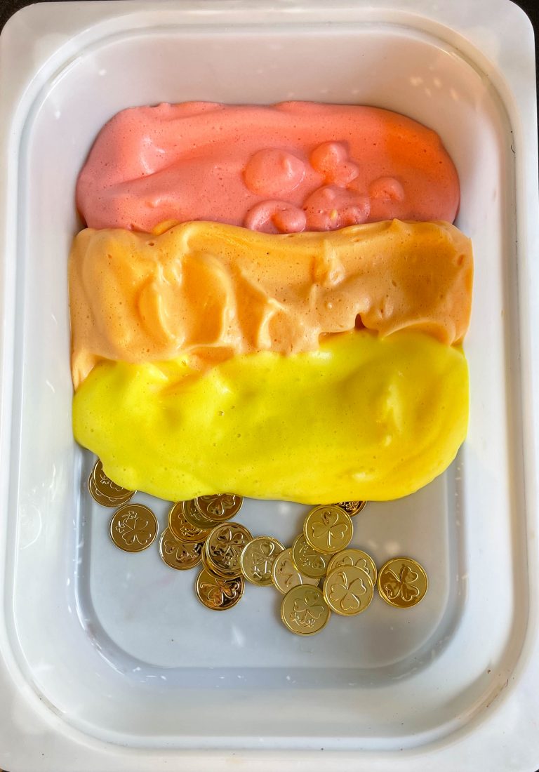 The setup of rainbow aquafaba sensory activity. Red, orange, and yellow foam covering gold coins. 